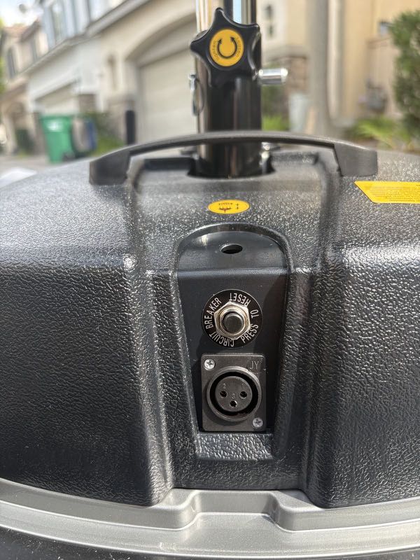 The charge port on the scooter, a round three-pin socket, with the circular circuit breaker button beside it